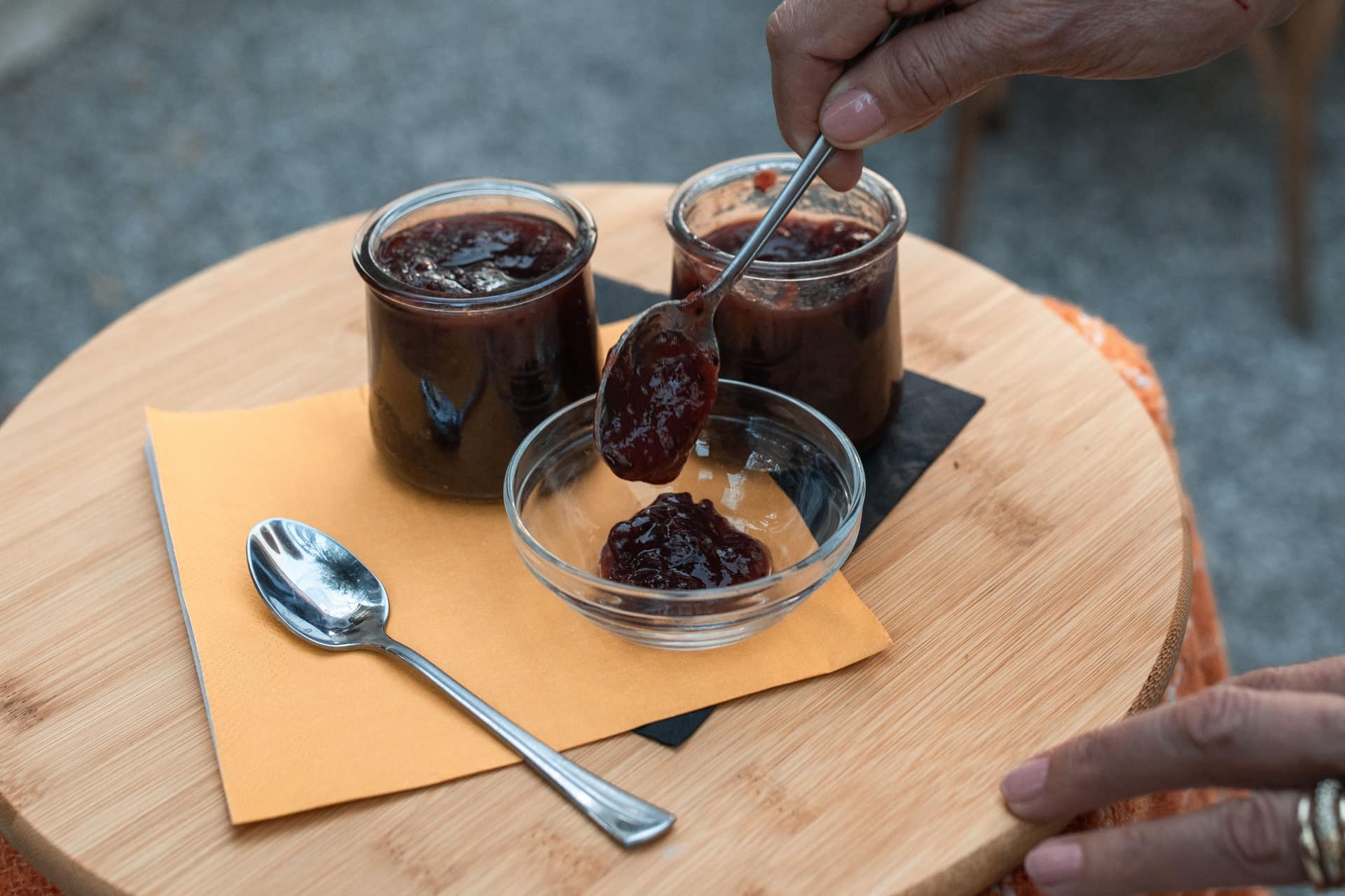 Hands transferring homemade jam from small jars into a bowl