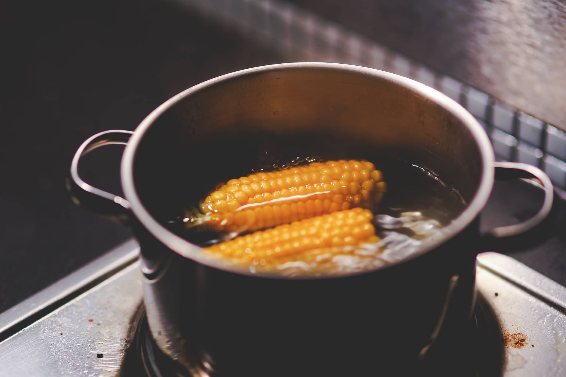 Corn cobs boiling in a stainless steel pot on a stove