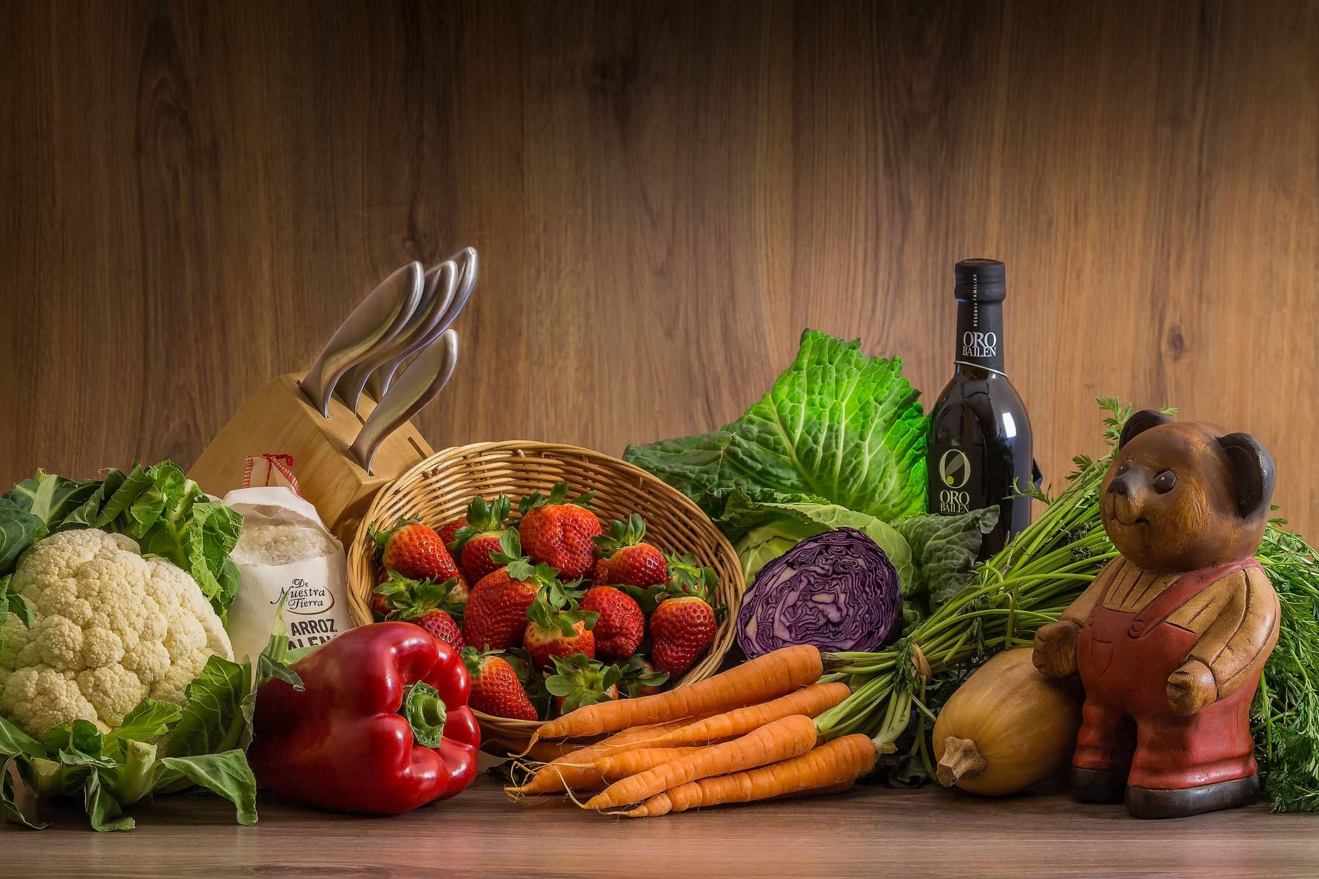 Fresh vegetables and fruit arranged on a wooden table with kitchen tools