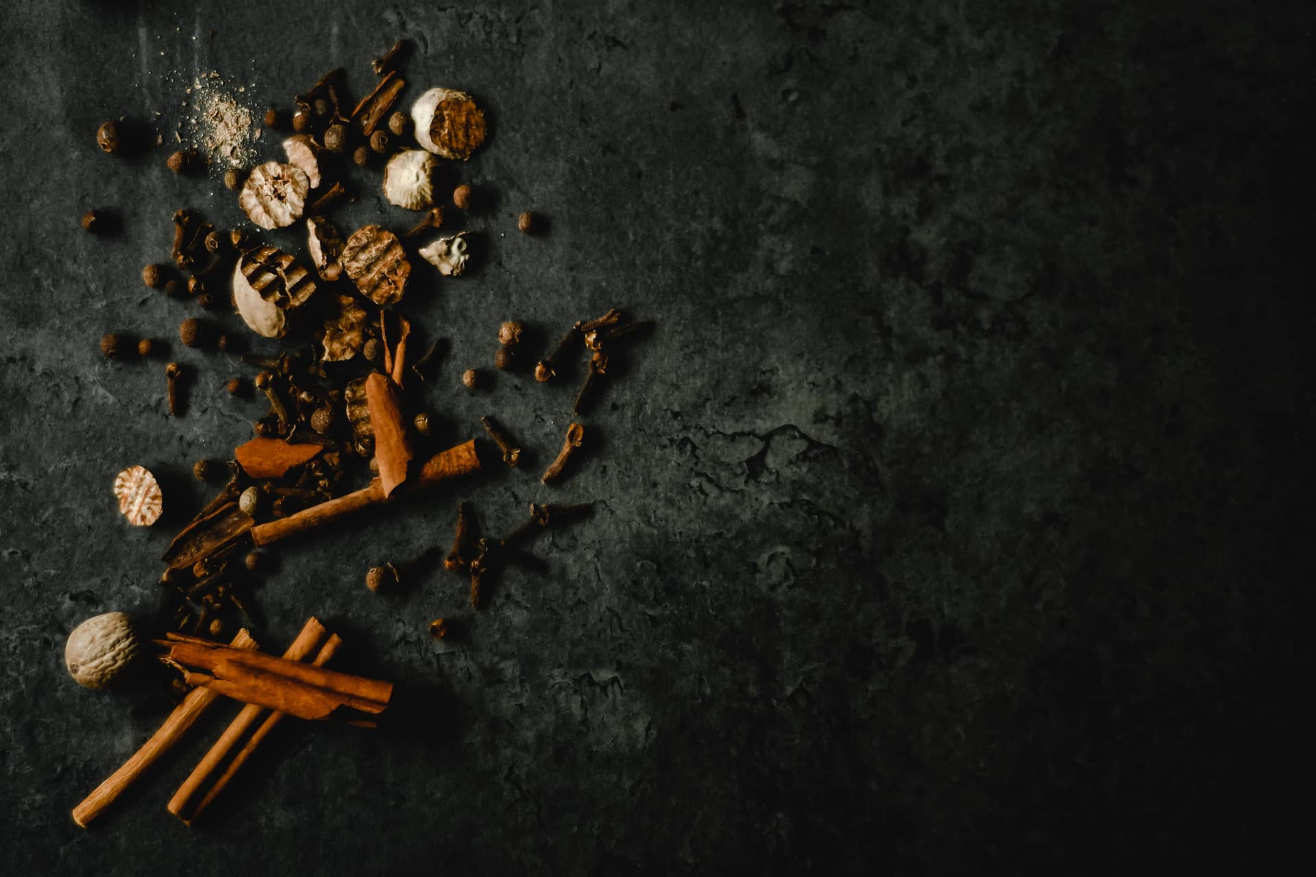 Whole spices including cinnamon and cloves on a dark counter
