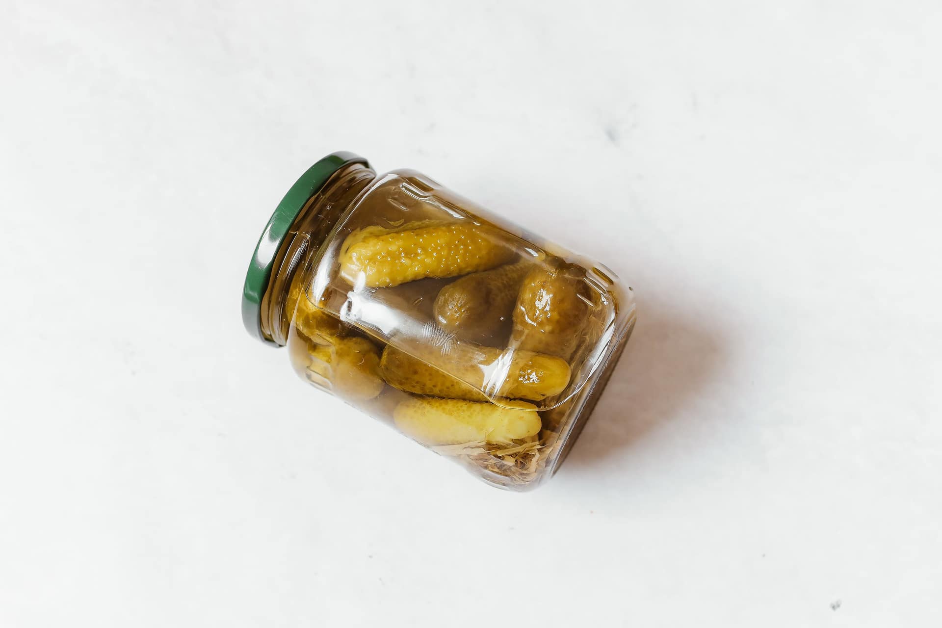 A glass jar of pickled cucumbers on a white surface