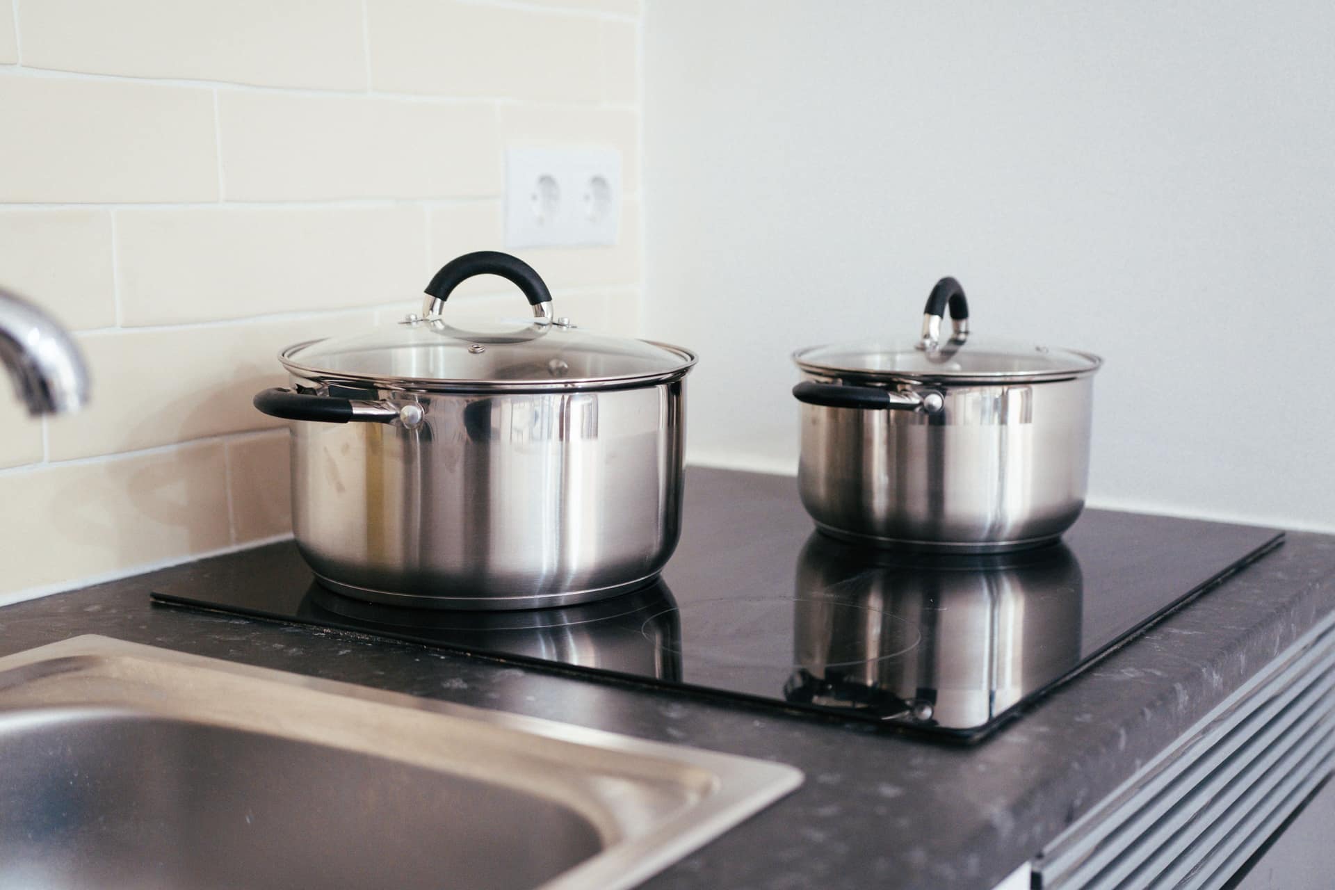 Stainless steel pots on a black induction cooktop in a modern kitchen