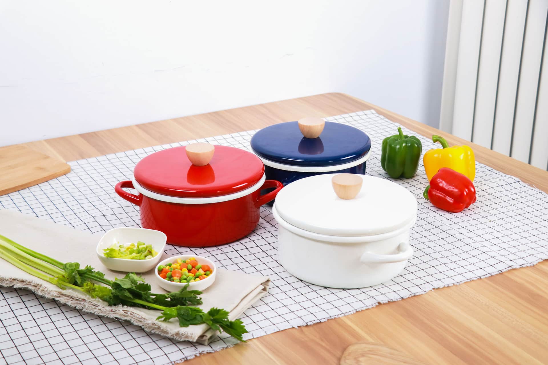 Enamel pots with colored lids on a table with fresh vegetables
