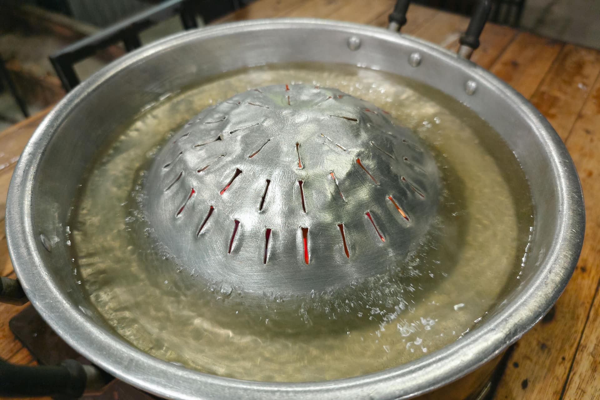 A metal pot of boiling water with steam rising in a kitchen