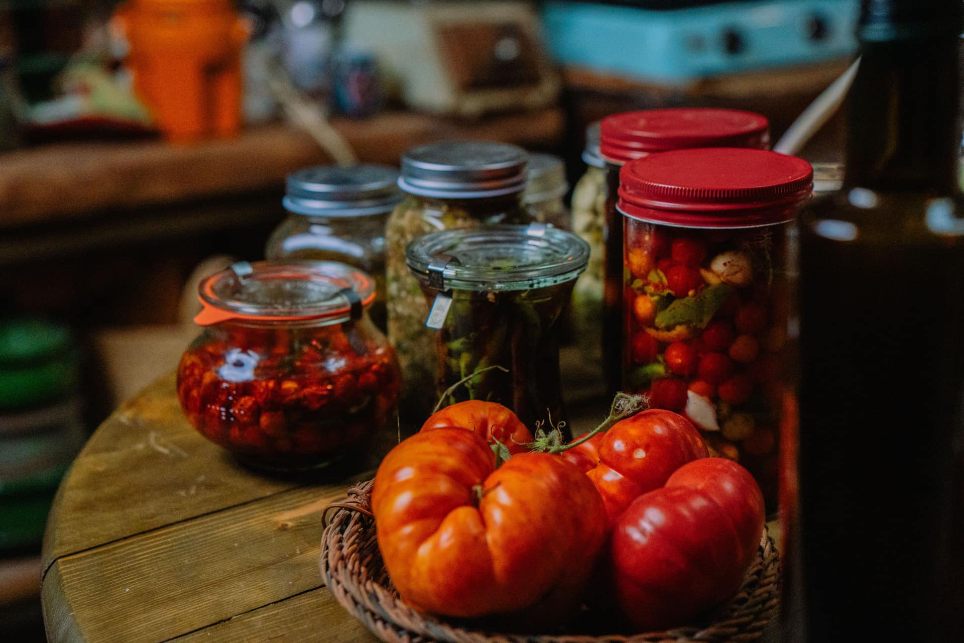 Fresh tomatoes and jars of pickled vegetables on a kitchen table